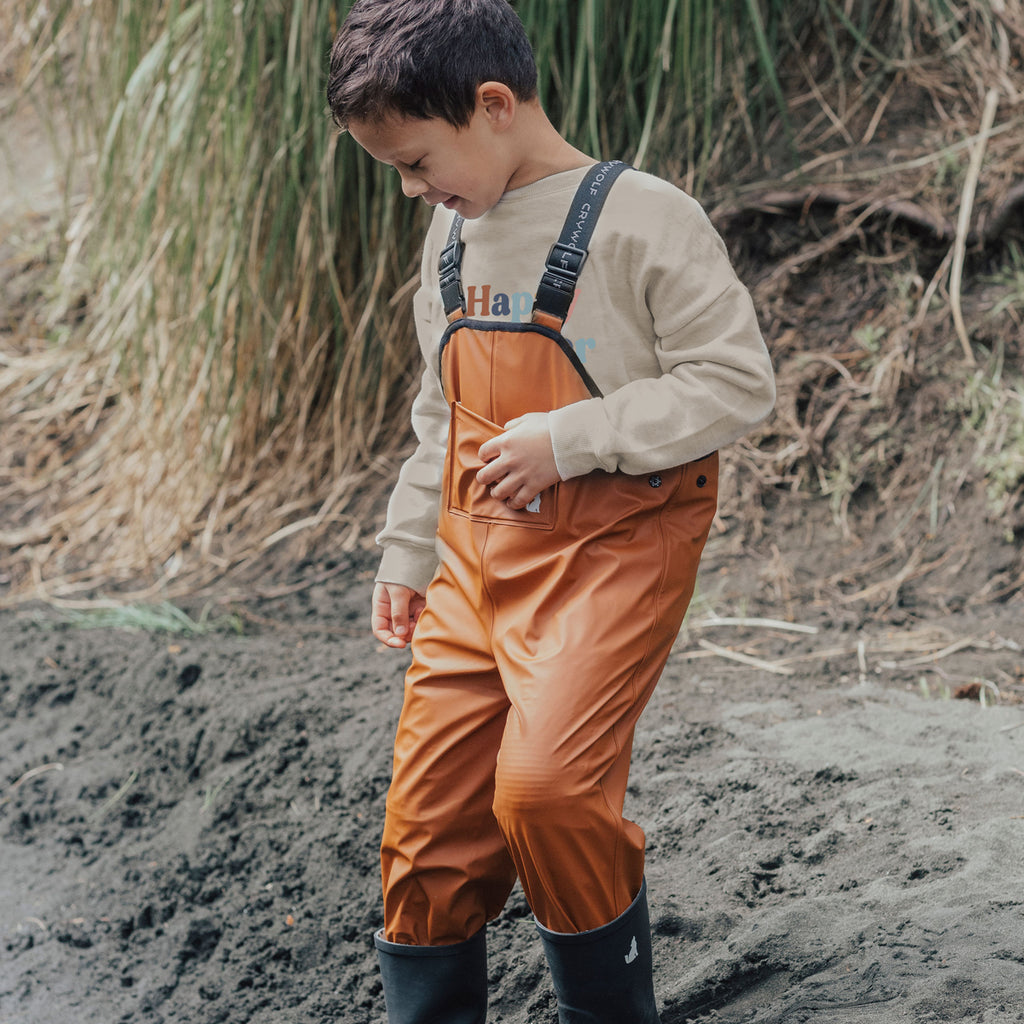 A Boy Outside Wearing Rain Overalls Rust Made From Recycled Fabrics - Front View