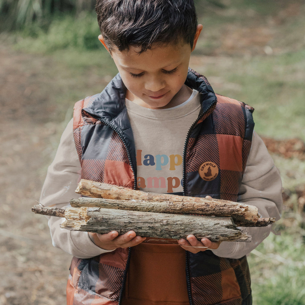 A boy carrying tree branches while wearing an organic sweater by Crywolf
